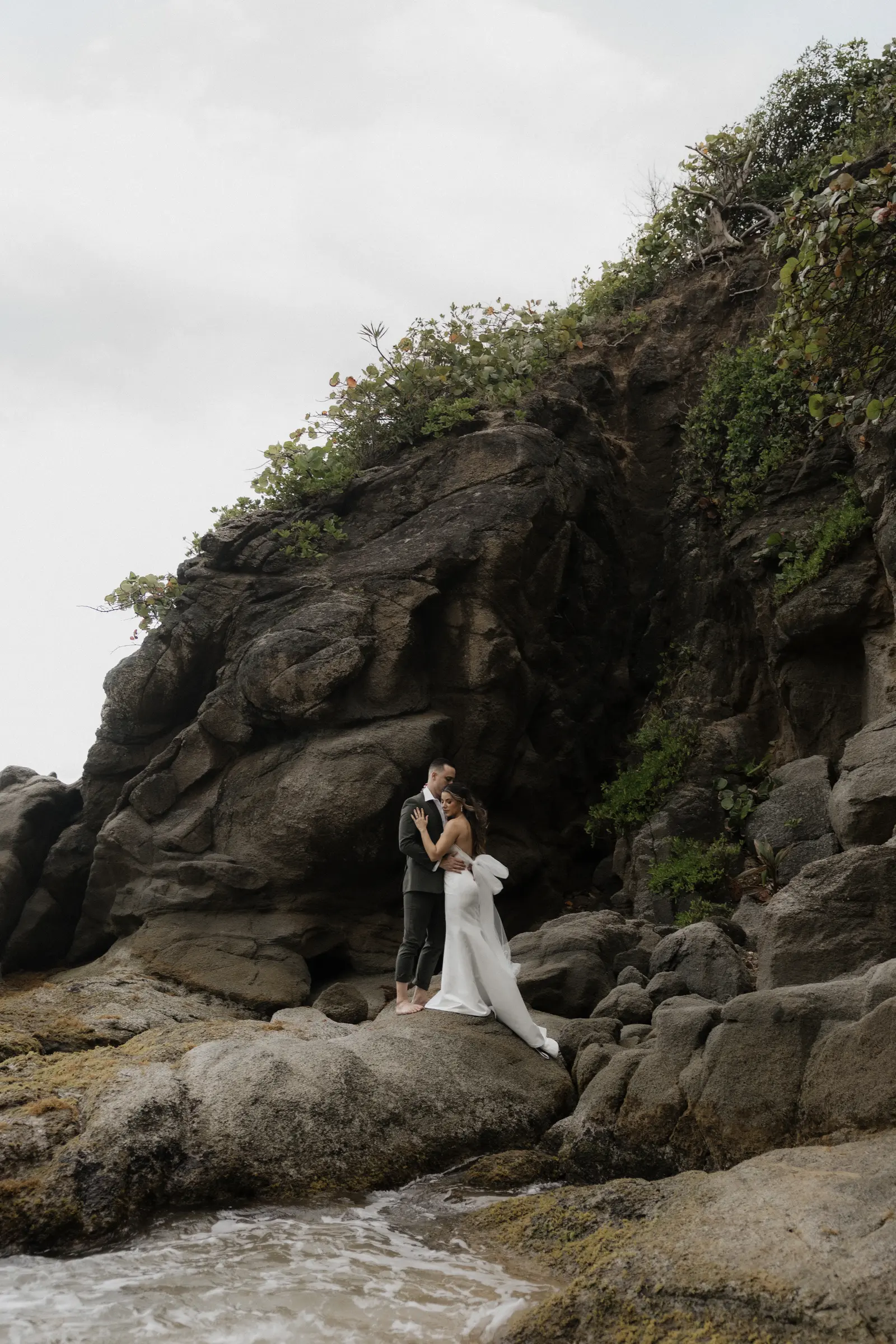 Bride and groom standing among coastal rocks