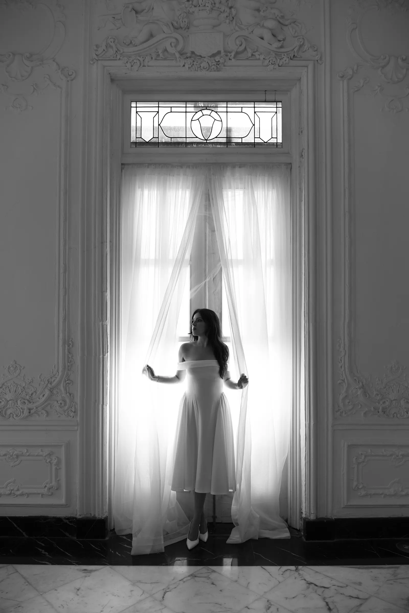 Bride silhouetted against a tall window with sheer curtains