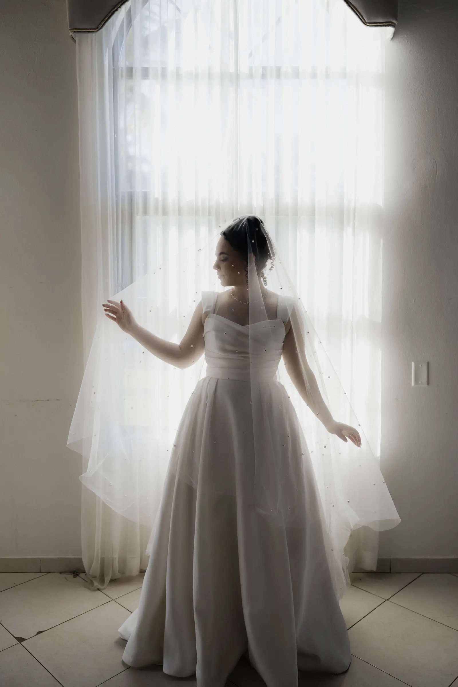Bride standing by a sheer-curtained window