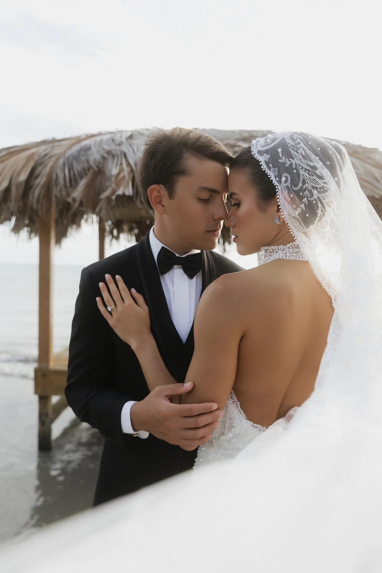 Bride and groom embracing under a palm-thatched pavilion