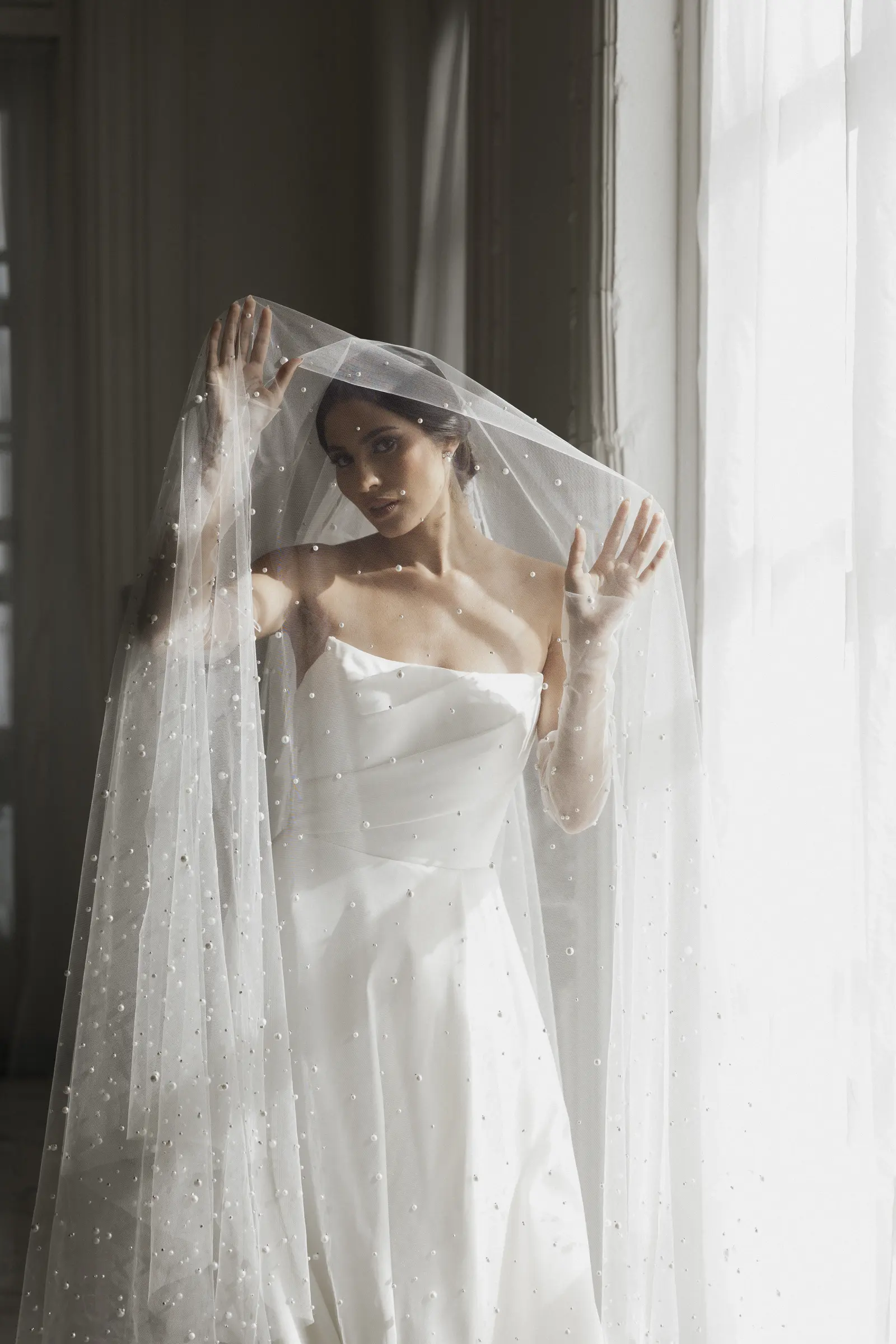 Bride adjusting her veil by a window