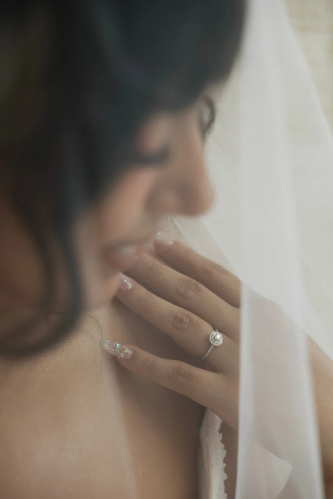 Close-up of a bride's engagement ring and hand beneath her veil