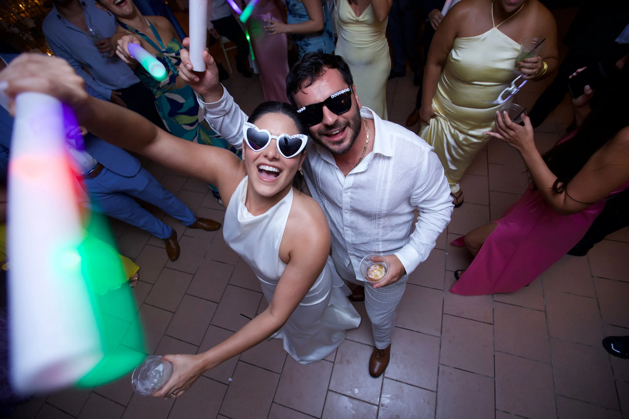 Bride and groom laughing on the dance floor wearing heart-shaped sunglasses at their reception
