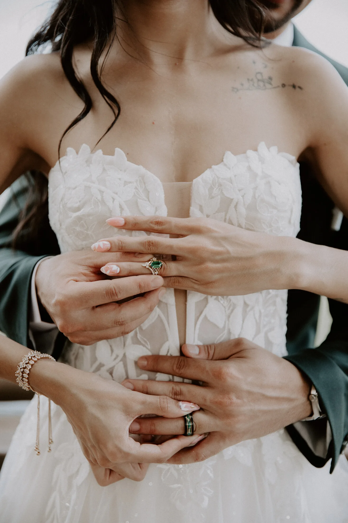 Close-up of a bride and groom's hands with wedding rings against lace gown detail