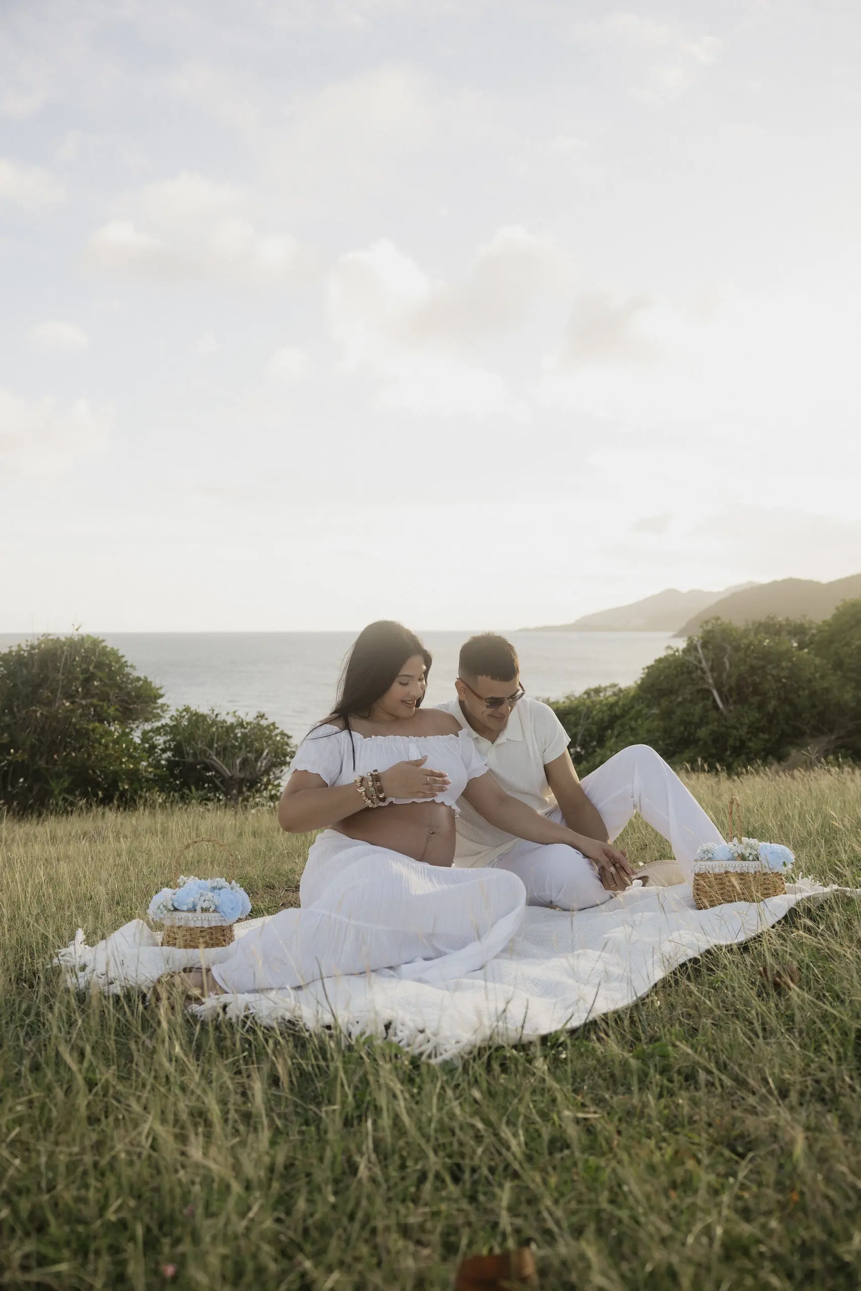 Pregnant couple sitting together in a grassy field at golden hour