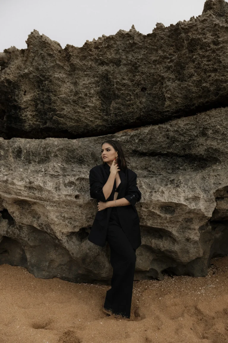 Woman in a black outfit leaning against coastal rocks