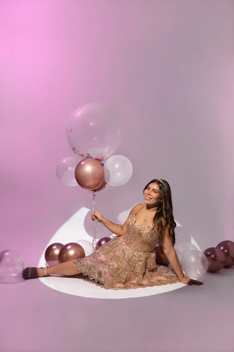 Woman in a gold dress reclining amid balloons in a glamour-style studio setup