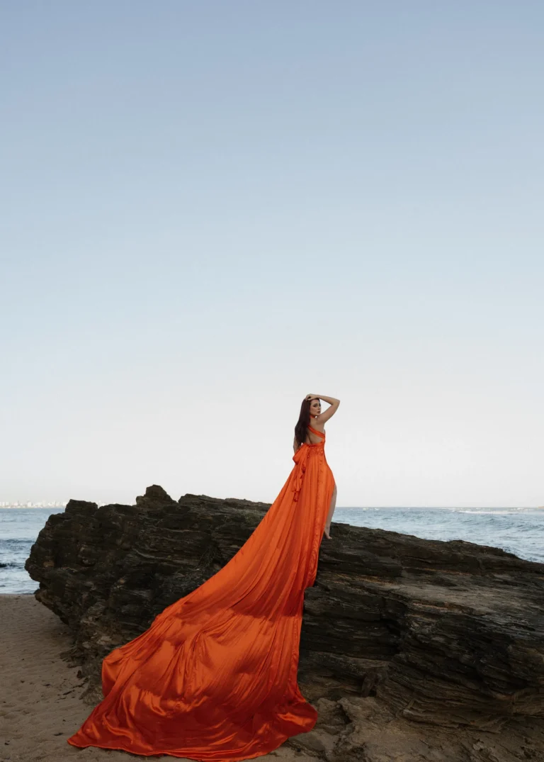 Woman in a flowing orange gown posed on coastal rocks