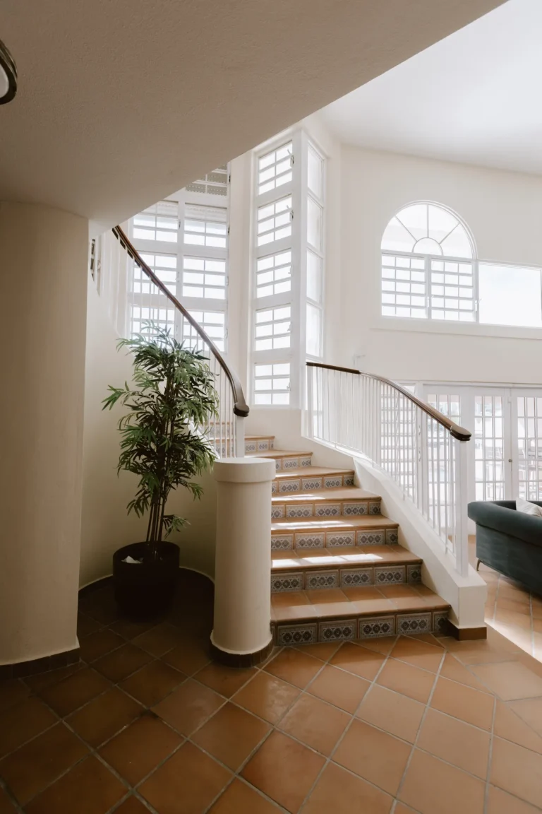Bright interior staircase with terracotta tile floor, iron railing, and a tall arched window